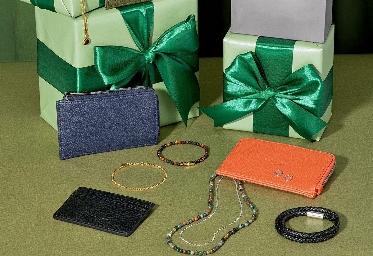 Collection of wallets, a cardholder, and bracelets on a green surface with gift boxes in the background.