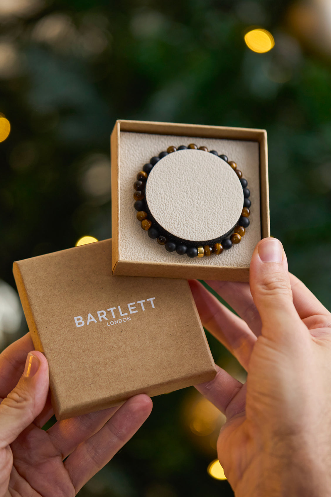 Person holding a bracelet in a 'Bartlett' box with a blurred green background
