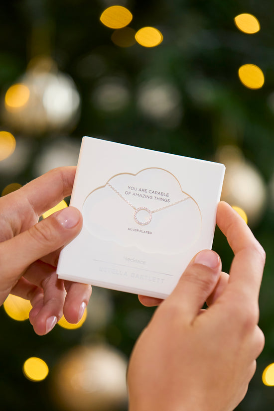 Two hands holding a white card with text against a blurred festive background