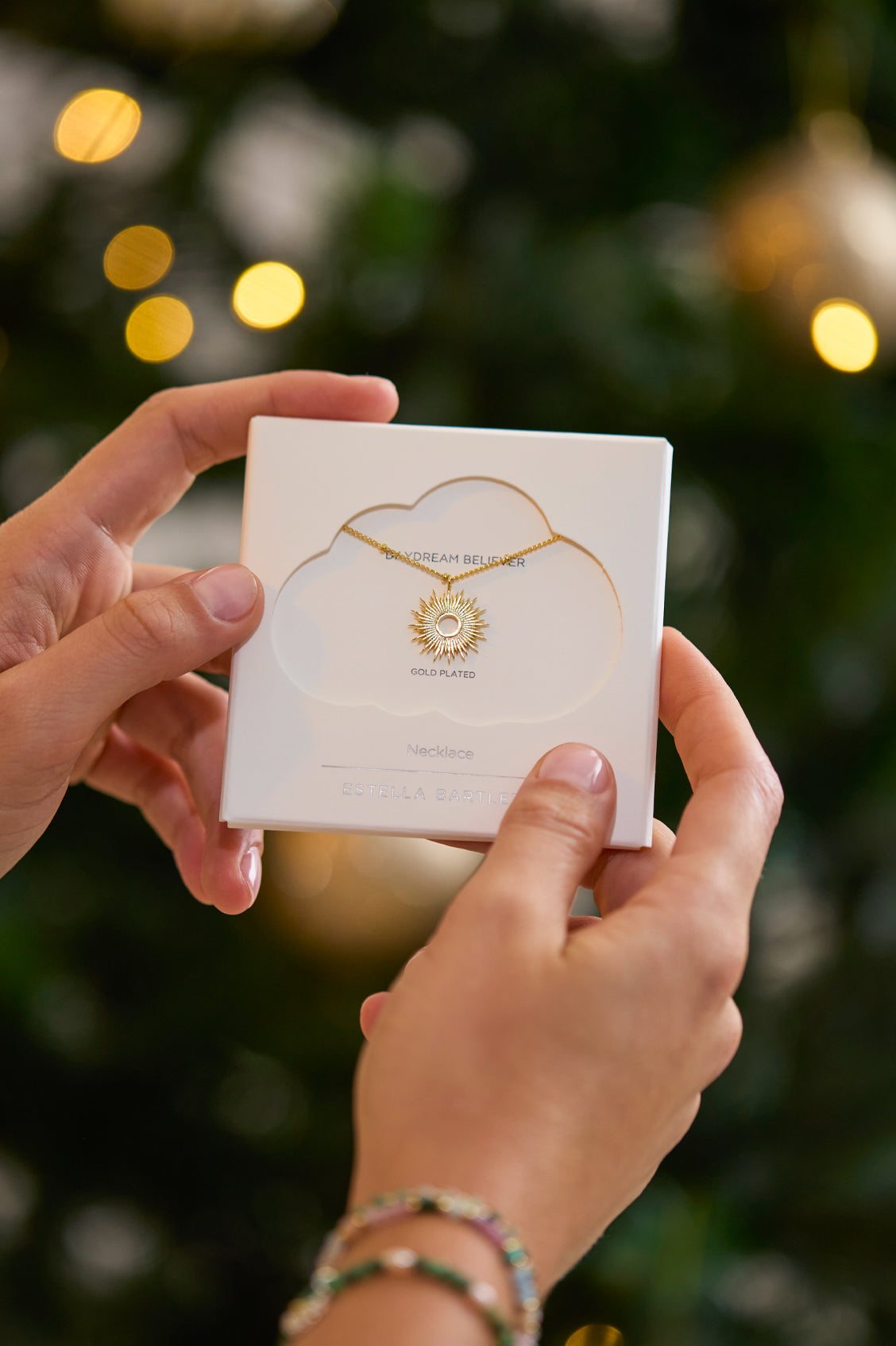 Person holding a jewelry box with a necklace design against a blurred Christmas tree background