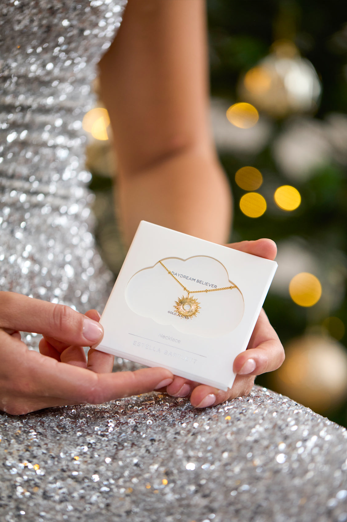 Person holding a jewelry box with a necklace design on a festive background