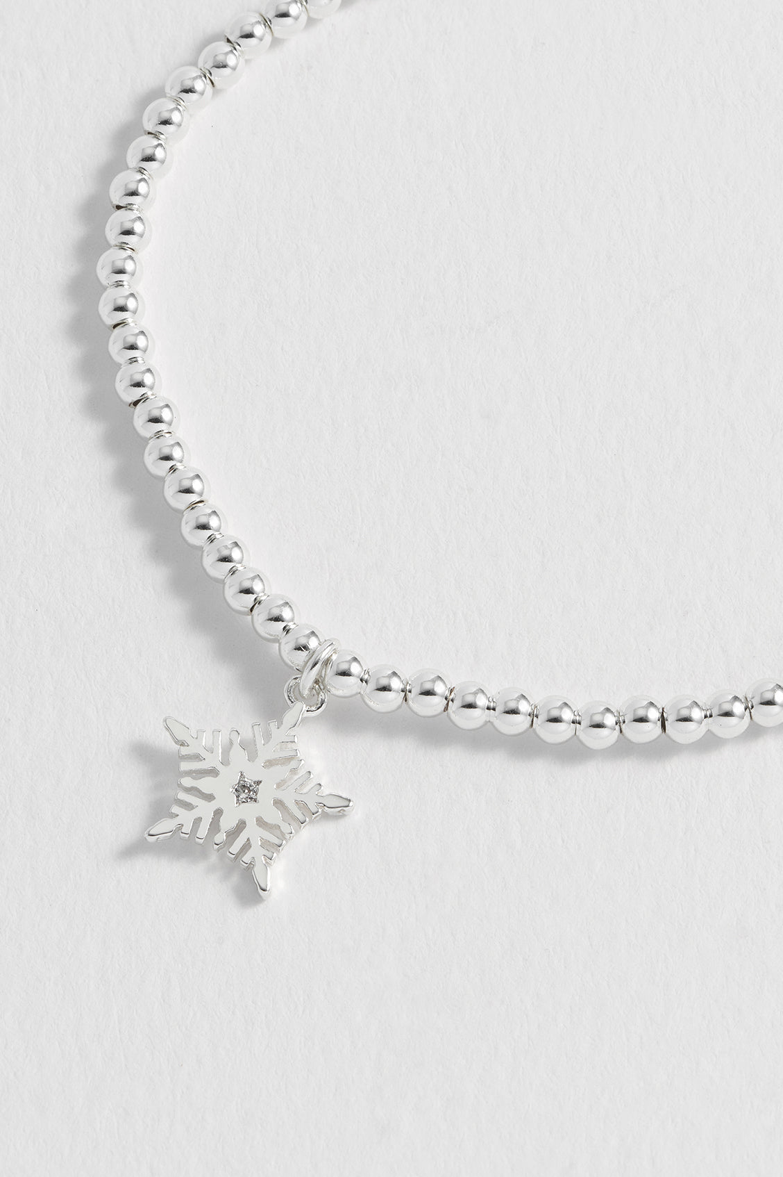 Silver beaded bracelet with a snowflake charm on a light gray background