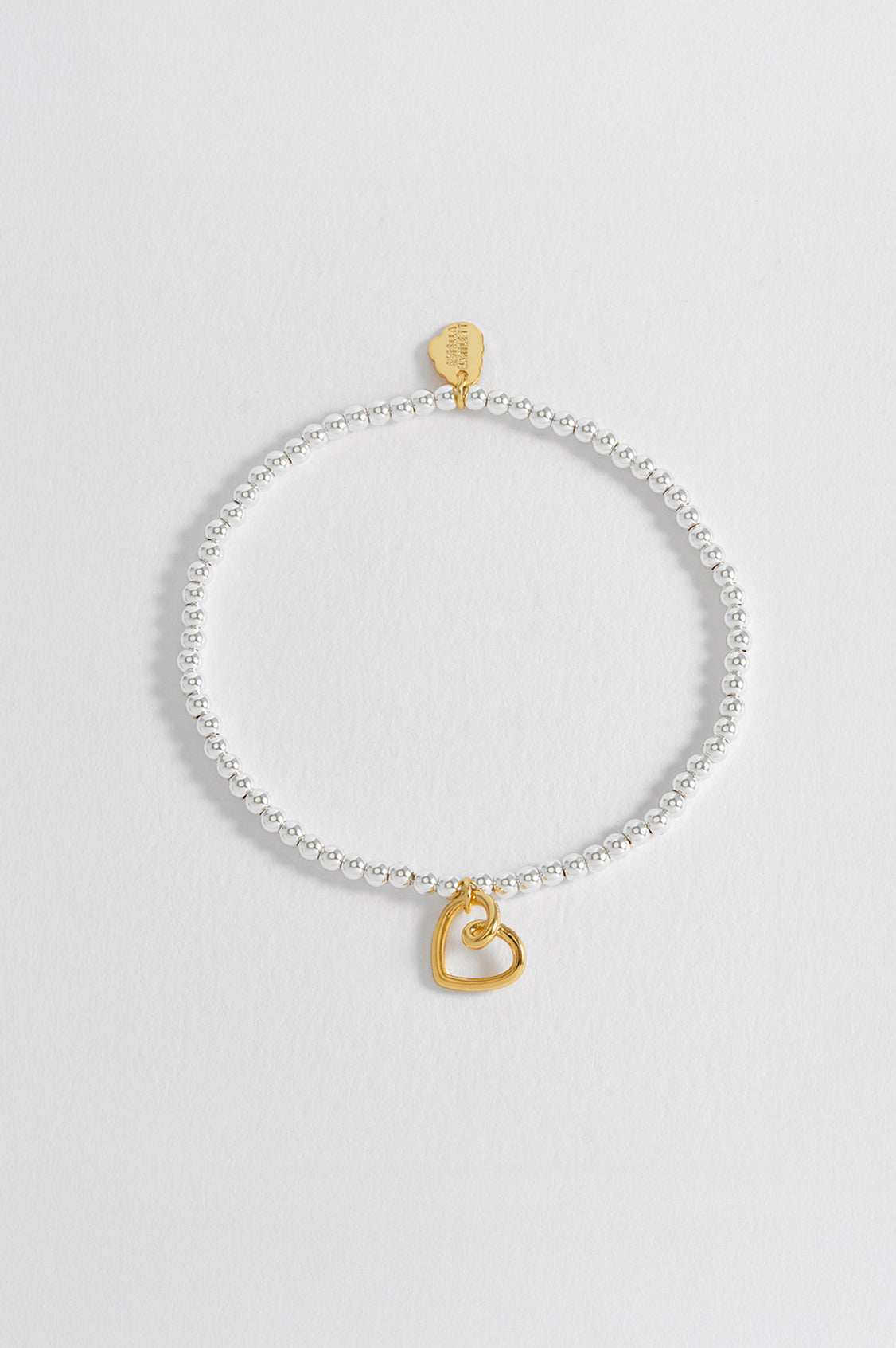 Silver bracelet with a gold heart charm on a light gray background
