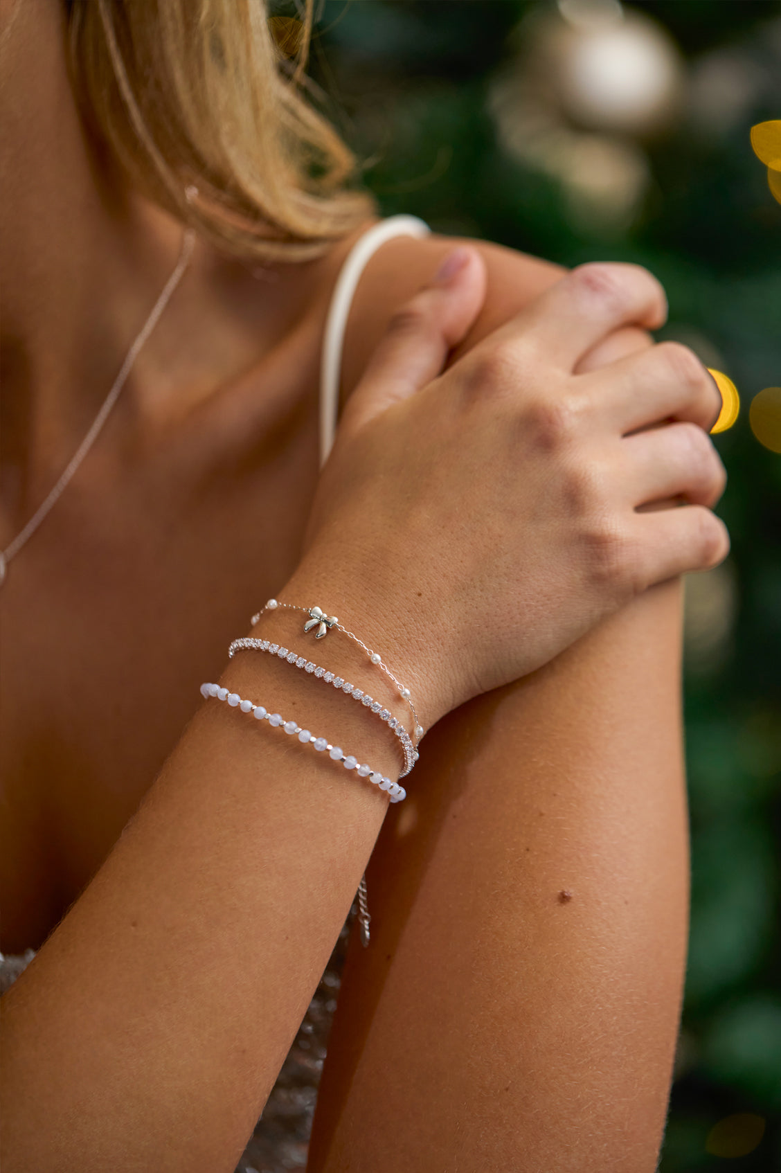 Close-up of a person's wrist with multiple silver bracelets against a blurred natural background