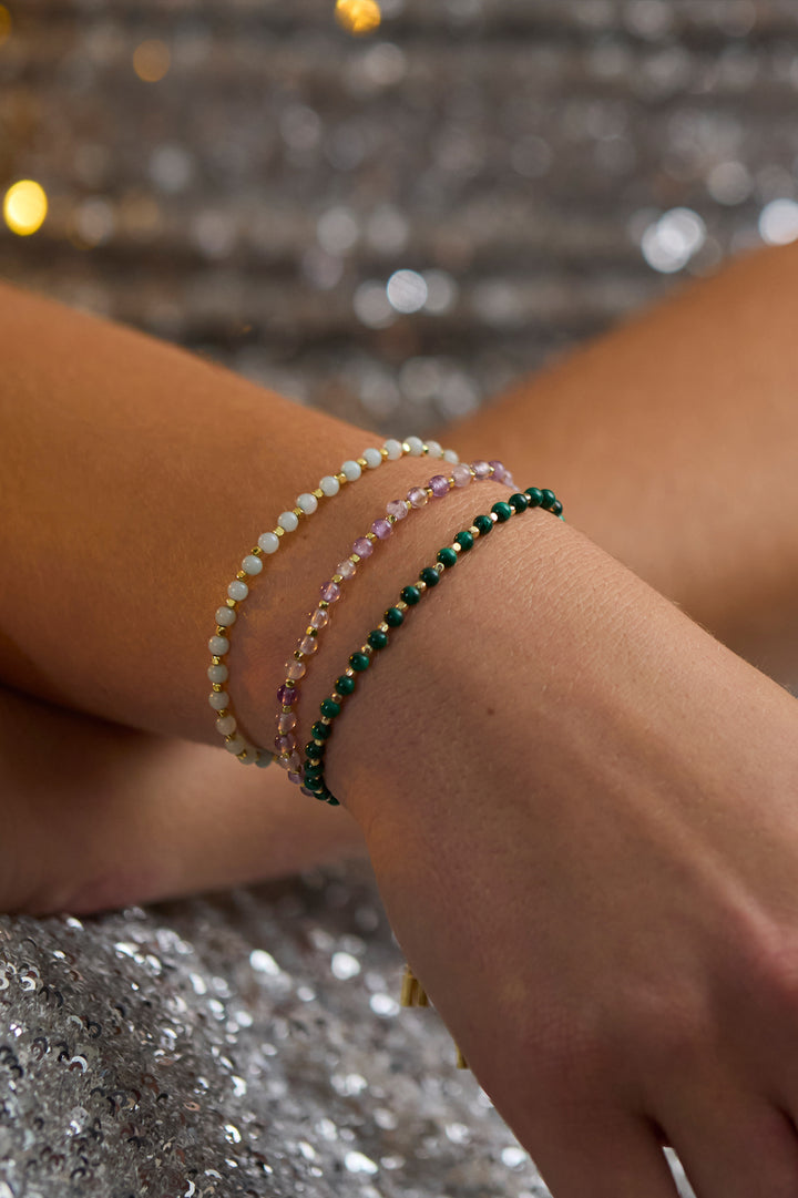 Close-up of a wrist wearing multiple beaded bracelets on a glittery surface.