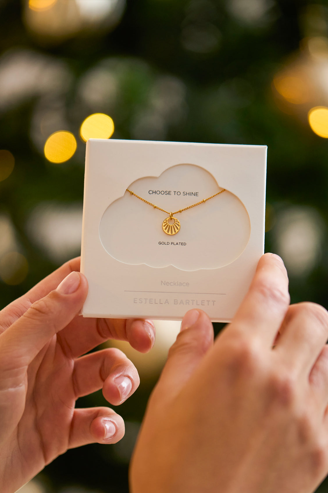 Gold necklace on a card held by hands with a blurred Christmas tree background
