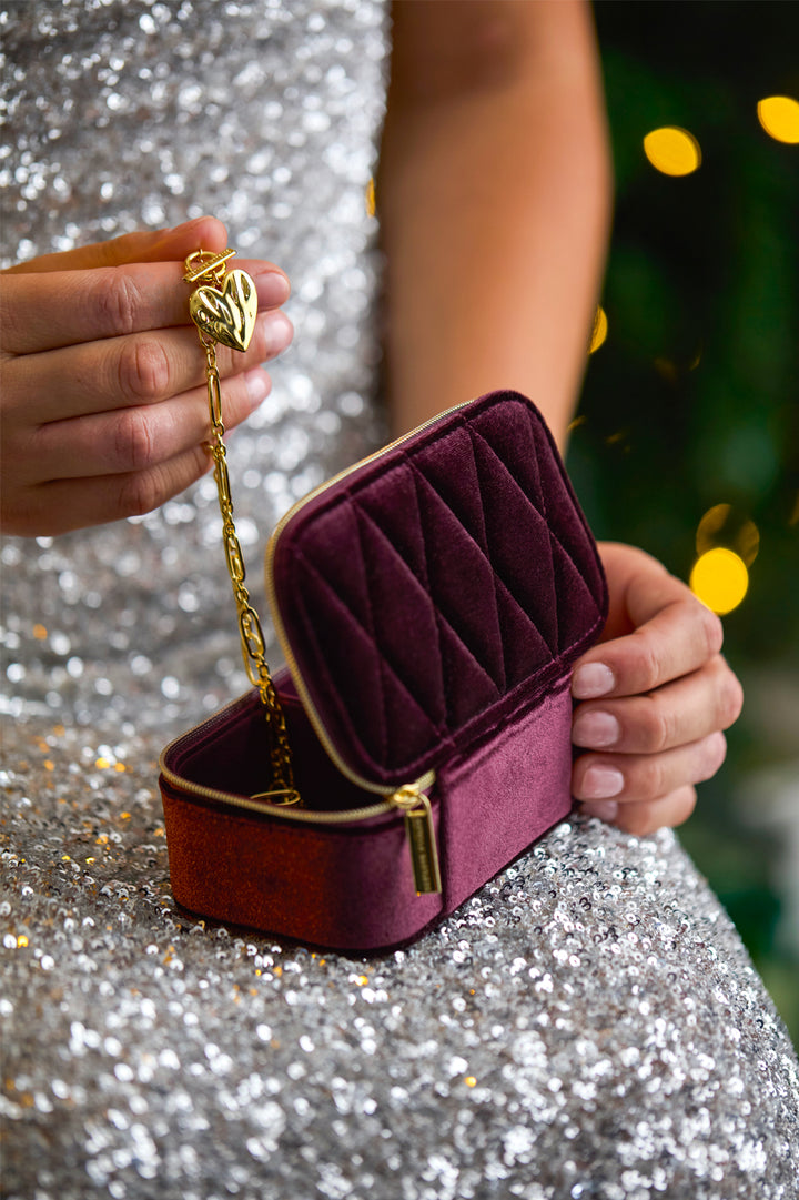 Person holding a burgundy velvet jewelry box with gold chain against a glittery background