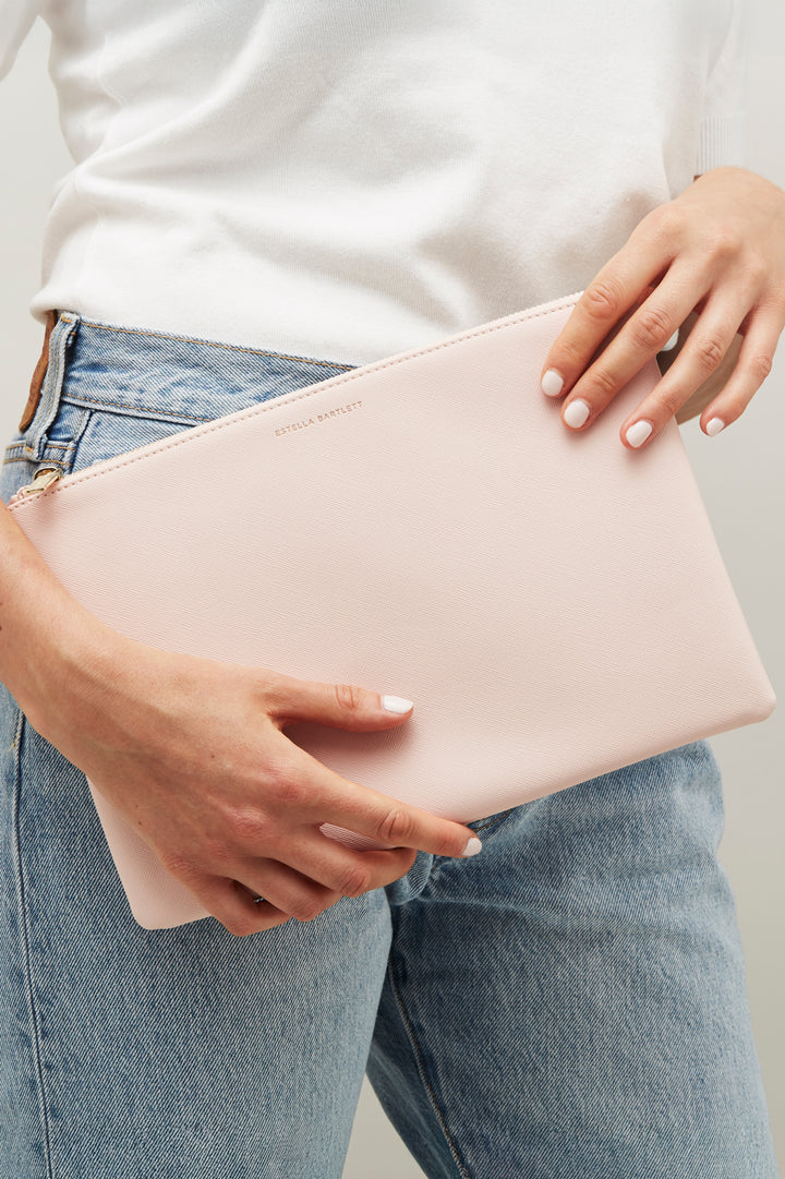 Person holding a light pink clutch with a neutral background