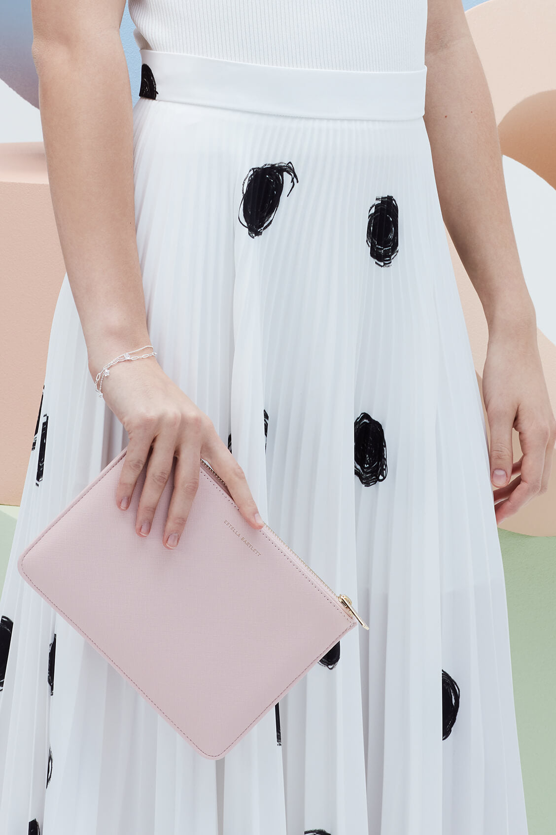 Person wearing a white dress with black polka dots holding a pink clutch.