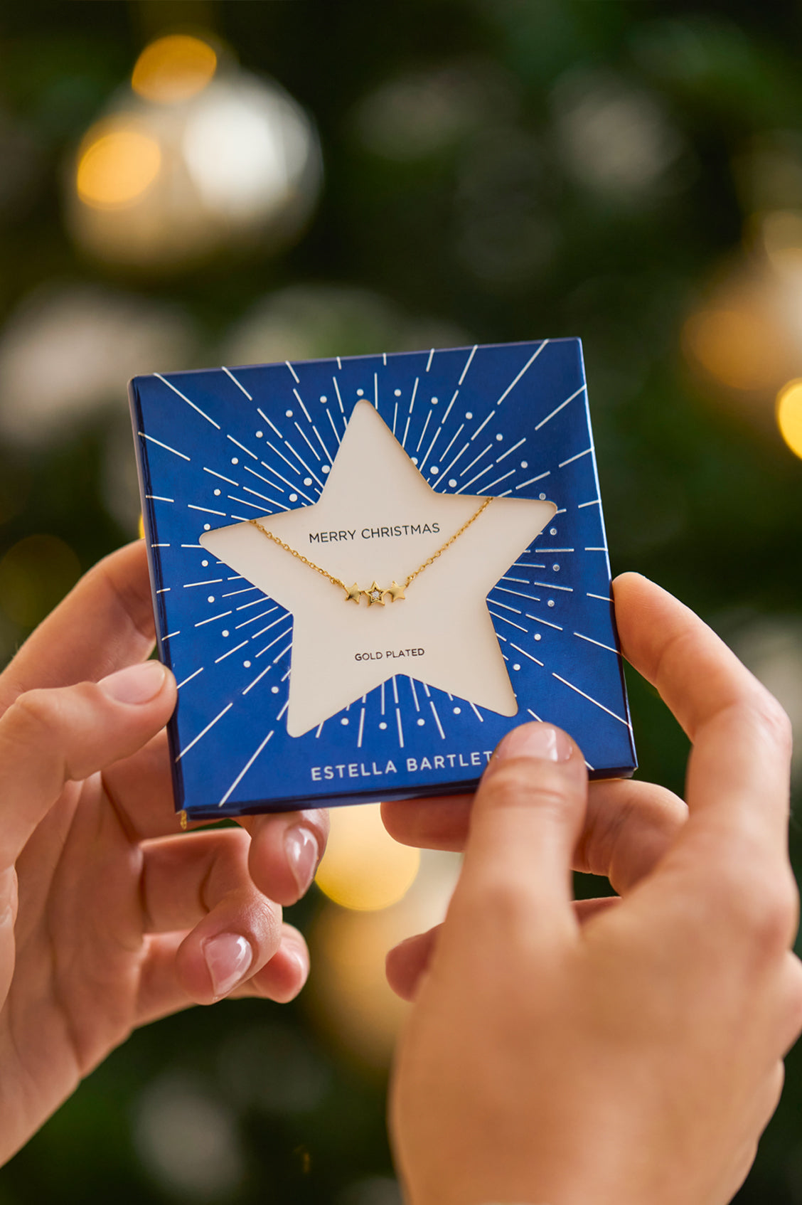 Star-shaped necklace in a blue box held by hands with a Christmas tree in the background