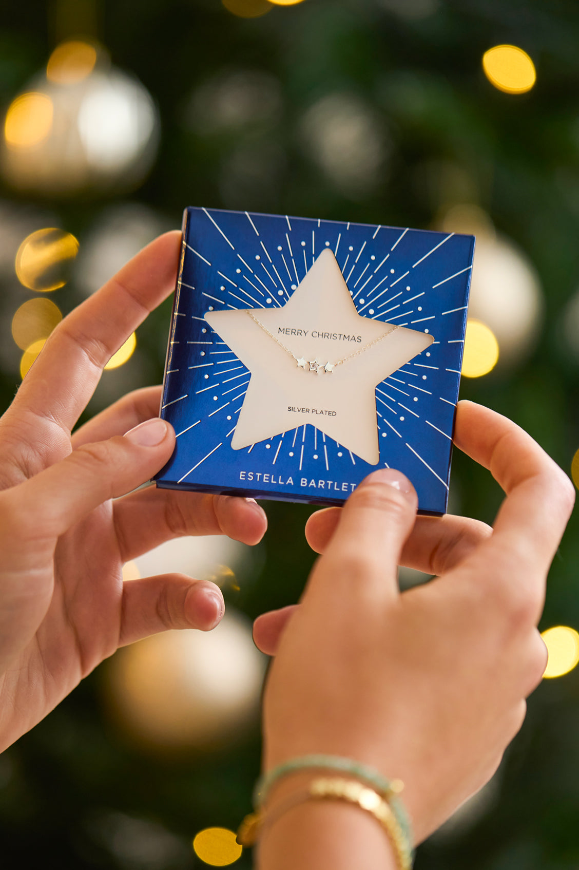 Blue Christmas gift box with star design held by hands against a blurred festive background