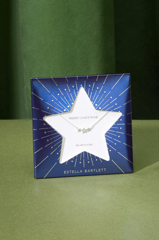 Star-shaped necklace on a blue card with 'Estella Bartlett' branding against a green background