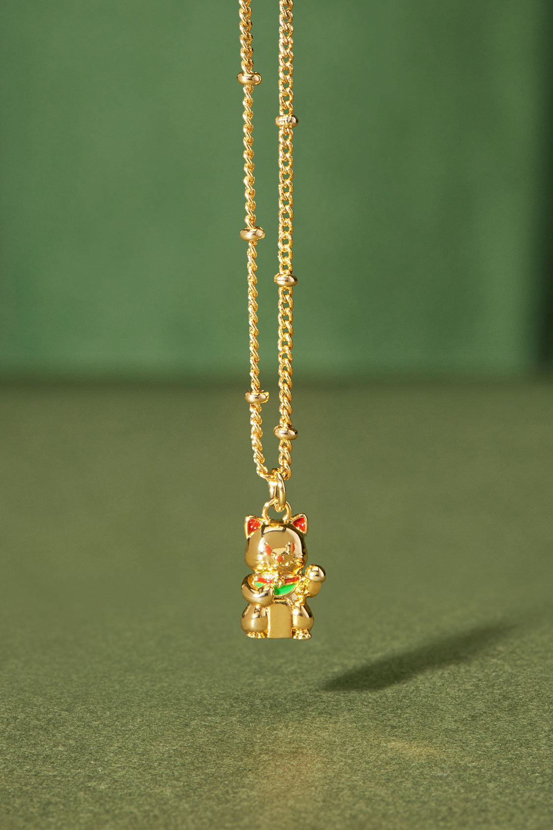 Gold necklace with a small pendant on a green background